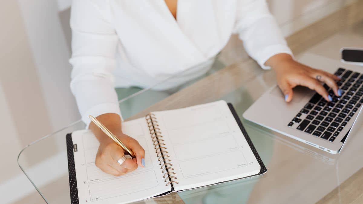 Writing domain name ideas in a notebook beside a laptop